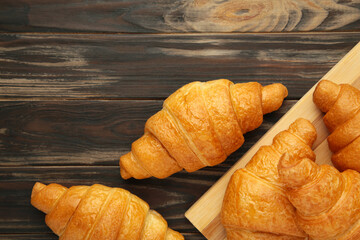 Freshly baked croissants on wooden cutting board on brown background.