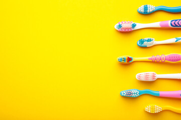 Colorful toothbrushes on yellow background with copy space