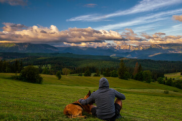 Fototapeta na wymiar Man and dog friends travel together on hike in tatra Mountains at summer sunset