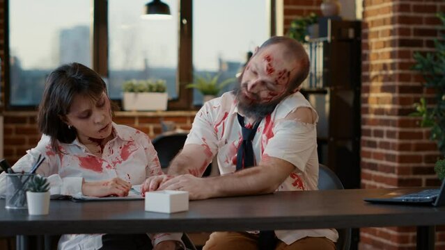 Spooky zombie proposing to his dead walking creepy girlfriend inside office. Brain-eating creepy looking evil monsters with deep and bloody wounds and scars getting married inside workspace