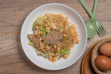 Stir fried vermicelli with pork, egg and collard greens in a white plate.