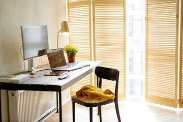 Cozy workplace with computers on wooden table in sunny room. Concept of home office
