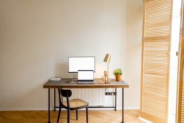 Workplace with computers on a wooden table in sunny room of stylish apartment. Mockup image with copy space on screens