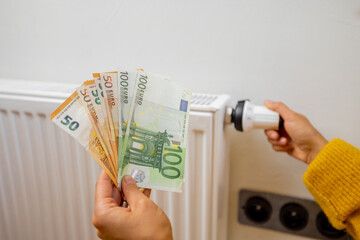 Person holding euro banknotes near heater at home. Concept of expensive energy resources and the...