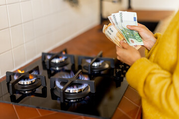 Person countes euro banknotes near burning gas stove at home. Concept of expensive gas and energy...