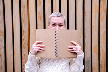 Woman hiding face behind open book in front of wall