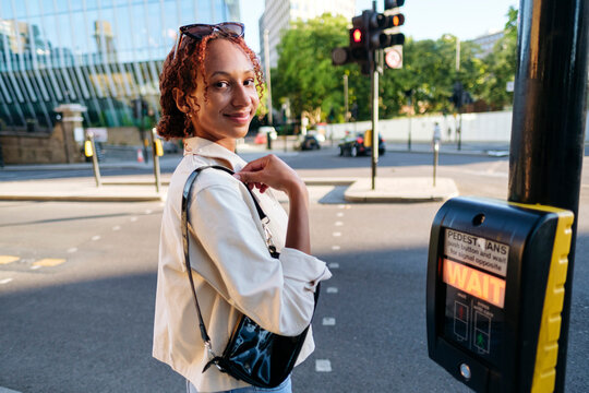 Smiling woman waiting by pedestrian crossing button