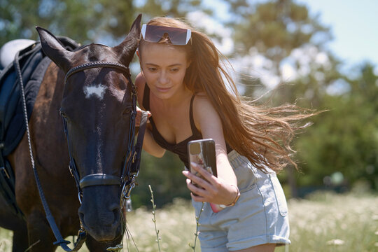 Beautiful woman with horse taking selfie through smart phone on sunny day