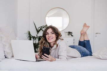 Thoughtful beautiful woman with laptop and smart phone lying on bed