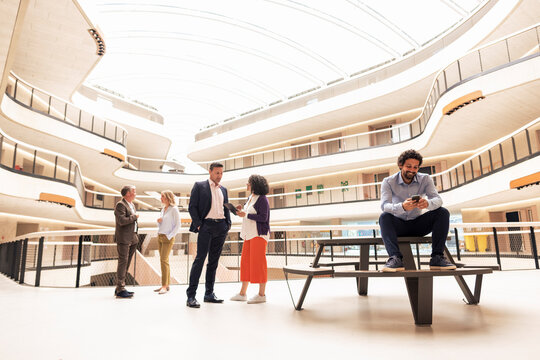Smiling businessman text messaging on smart phone with colleagues in background
