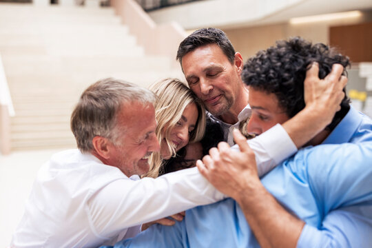 Happy senior businessman embracing colleagues in lobby