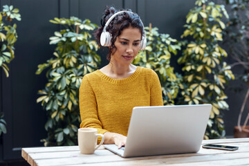 Businesswoman listening music through headphones working on laptop at cafe