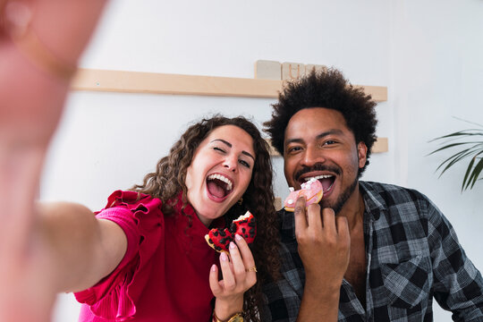 Happy young businesswoman enjoying doughnut with colleague in cafeteria