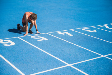 Young athlete kneeling at starting line on sunny day