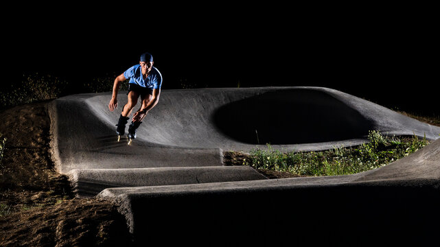Young man practicing inline skating in skateboard park at night