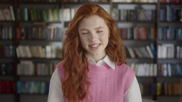 Happy Positive Red-haired Young Woman Laughing at Funny Joke Looking at Camera in Library. Cheerful Female Teen School College Student Having Fun, Smiling Face Close Up Portrait.