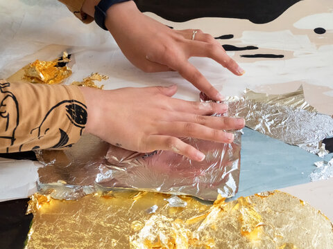 Female hands apply gold and silver potal to the picture. Potal painting technique, applying gold leaf particles to an interior painting.