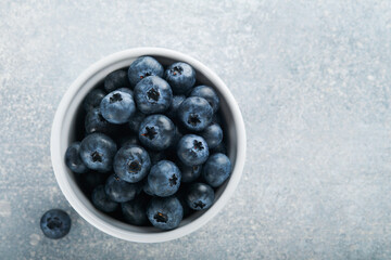 Blueberry. White bowl of fresh blueberries on grey stone background table. Tasty ripe blueberries. Place for text. Food background. Top view.