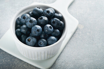 Blueberry. White bowl of fresh blueberries on grey stone background table. Tasty ripe blueberries. Place for text. Food background. Top view.