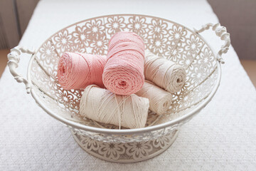 Handmade macrame braiding and cotton threads in basket on white background. Cotton macrame cords and ropes against wire basket. Good image for macrame and handicrafts banners and advertisement.