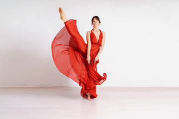 Dancer in a red flying dress. Woman ballerina dancing on a white studio background