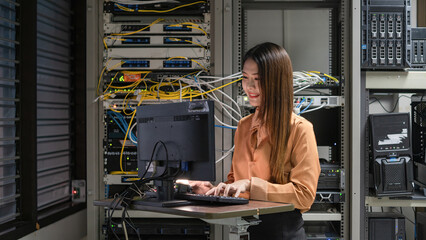 A female programmer is working in a server room. The girl is standing next to the computer racks of...