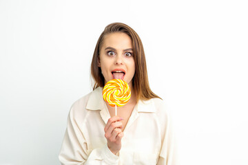 Beautiful young caucasian woman wearing a white shirt licking a lollipop on a white background