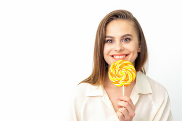 Beautiful young caucasian woman wearing a white shirt licking a lollipop on a white background