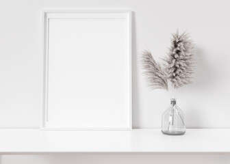 Empty vertical picture frame standing on white shelf. Frame mock up. Copy space for picture, poster. Template for your artwork. Close up view. Pampas grass in vase. 3D rendering.