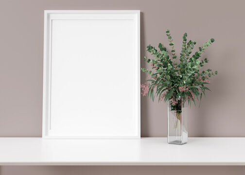Empty vertical picture frame standing on white shelf. Frame mock up. Copy space for picture, poster. Template for your artwork. Close up view. Eucalyptus plant in vase. 3D rendering. © Creative_Bird