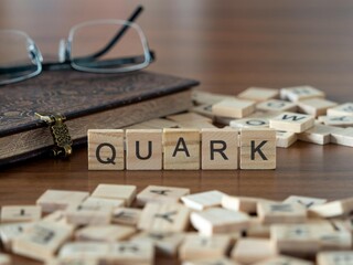 quark word or concept represented by wooden letter tiles on a wooden table with glasses and a book
