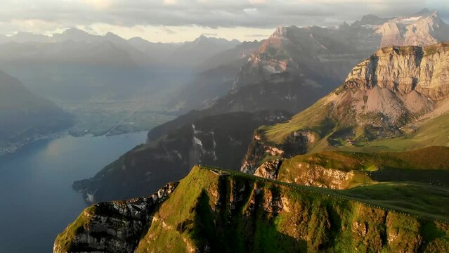 Aerial flight around the summit of Niederbauen Chulm on a golden summer morning in the Swiss Alps with a spinning view of the fjords of Lake Lucerne, Uri, Mythen, Rigi, Burgenstock and the rising sun