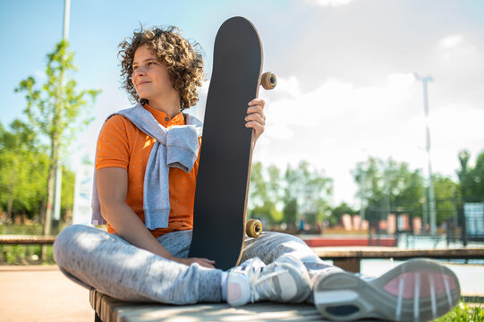 Pleased boy with the skateboard sitting in the park