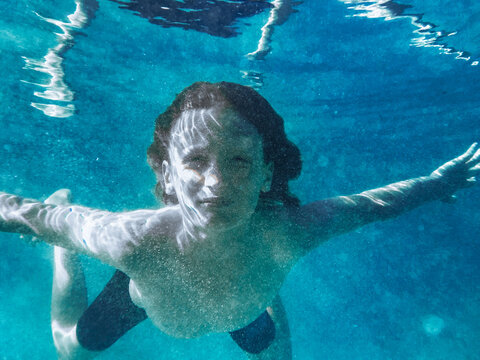 Young boy swimming underwater in blue ocean looking at camera