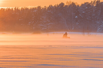 Amazing winter sunset in the forest with the orange sky, and snowmobile driving in the mist