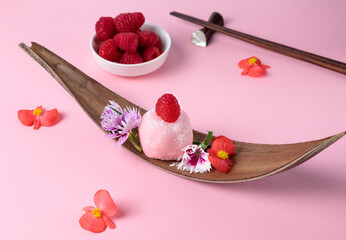 Raspberry mochi on a wooden stand, decorated with edible flowers and berries. Close-up.
