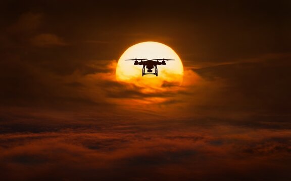 Silhouette of flying quadcopter against background of glowing sun