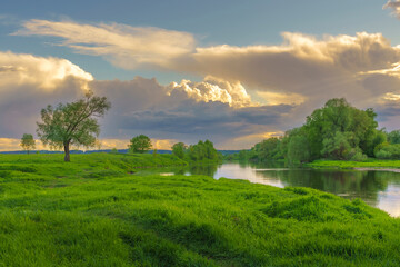 Summer landscape with river, green shores, and clouds in the sky at sunset