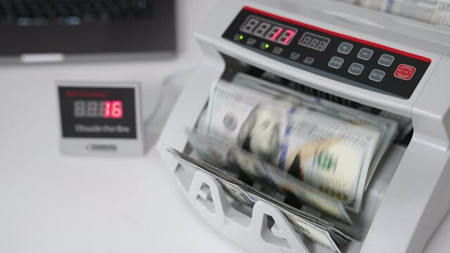Electronic money counting machine on the white table. UDS dollars calculated in the financial equipment. High angle view. Close up.