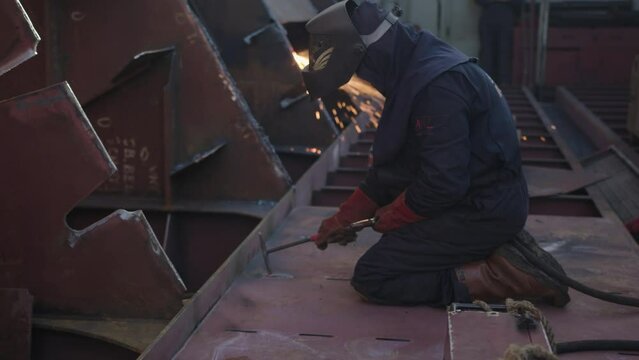 man working on a cargo ship is hammering a spot he just welded to make it's form good.