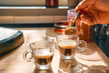 Hand of man putting brown sugar into cups with aromatic hot drink espresso, prepared in espresso...