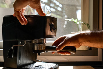 Hands of man making espresso in espresso coffee machine in the kitchen at home. Awakening hot...