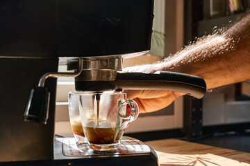 Hands of man making espresso in espresso coffee machine in the kitchen at home. Awakening hot drink. Morning habit.