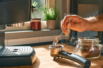 Hands of man making espresso in the kitchen, filling funnel of espresso coffee machine pot with...