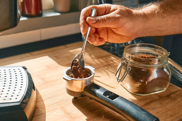 Hands of man making espresso in the kitchen, filling funnel of espresso coffee machine pot with ground coffee. Morning habit.