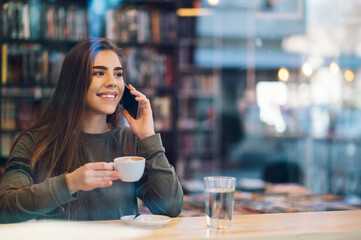 Woman using smartphone and drinking coffee in a cafe.