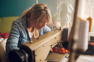 Tailor woman sitting and sewing on a sewing machine a in studio