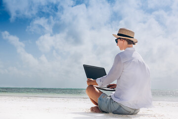 woman using and typing on laptop computer while sitting on the beach