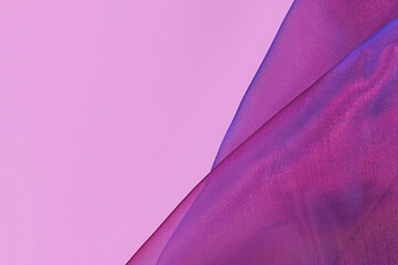 Purple tulle netting fabric with blue hue on side of pink background with copy space