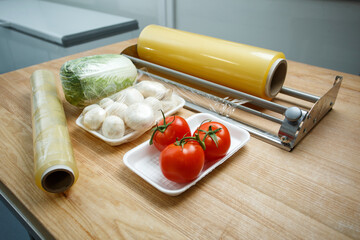 Close up of vegetables on white plastic trays lie on table near roll of stretch film.